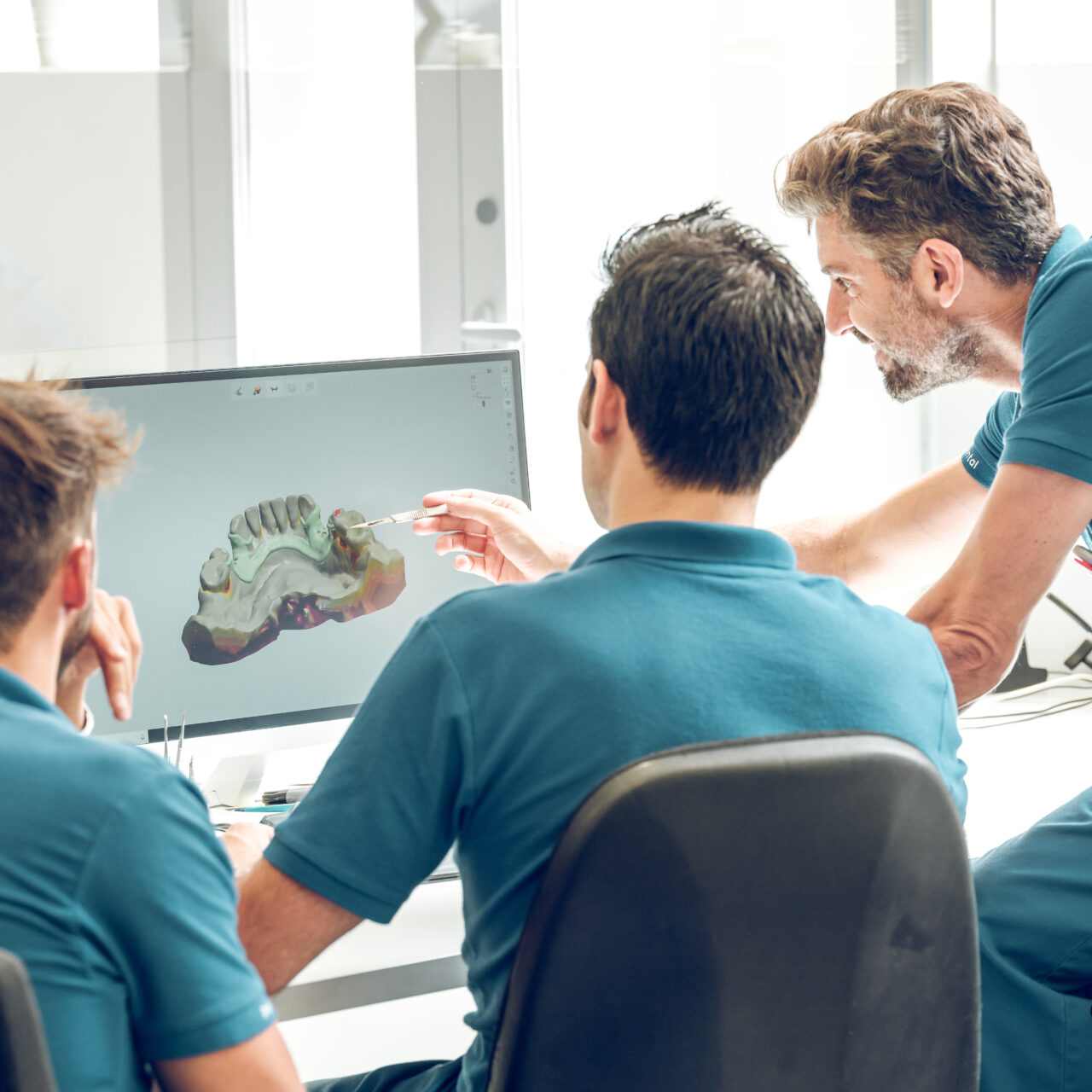 Back view of unrecognizable male pointing at monitor with 3d jaw model while working with colleagues in light contemporary workspace