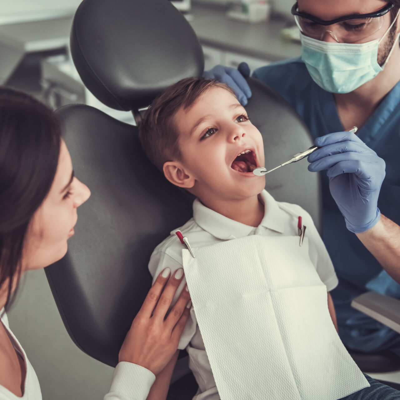 Cute little boy at the dentist. Mom is supporting her son while doctor is treating his teeth