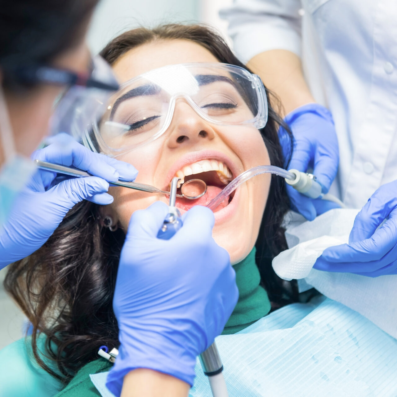 Two dentists busy with patient. Person in dental safety glasses.